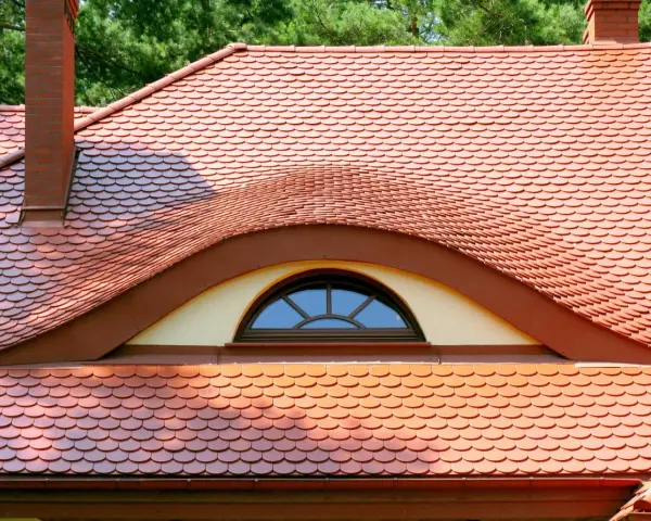 Dachówki ceramiczne w kolorze ceglastym pokrywają dach z charakterystycznym lukarną w kształcie oka.