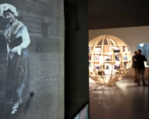 Exposition Albert Kahn : une femme en costume traditionnel sur une photo ancienne, un globe de bois rempli de clichés en arrière-plan.