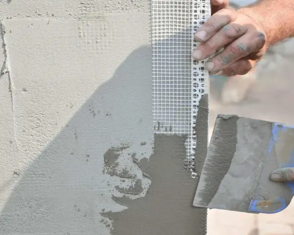 Mani esperte applicano stucco e rete per stuccare angolo muro, garantendo una finitura perfetta.