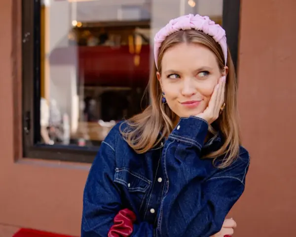 Aesthetic girl w jeansowej kurtce i różowej opasce na głowie, opiera policzek na dłoni, patrząc w bok.