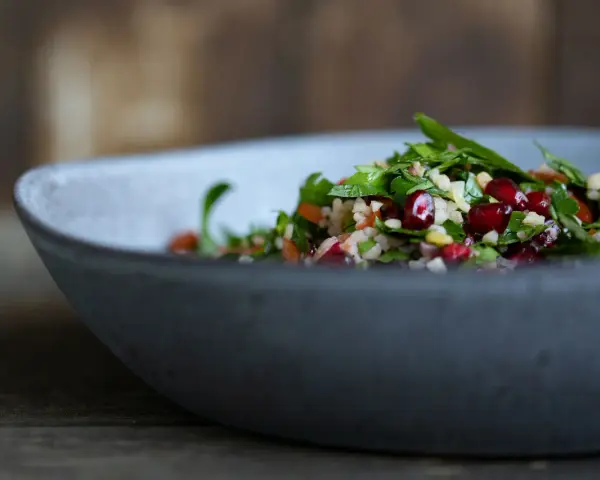 Frischer Tabouleh-Salat mit Granatapfelkernen in einer grauen Schüssel. Ein köstliches Rezept für den Sommer.