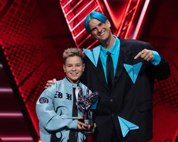 Chłopiec z błękitną kurtką i trofeum w kształcie dłoni, obok mężczyzny z niebieskimi włosami. To on wygrał The Voice Kids!