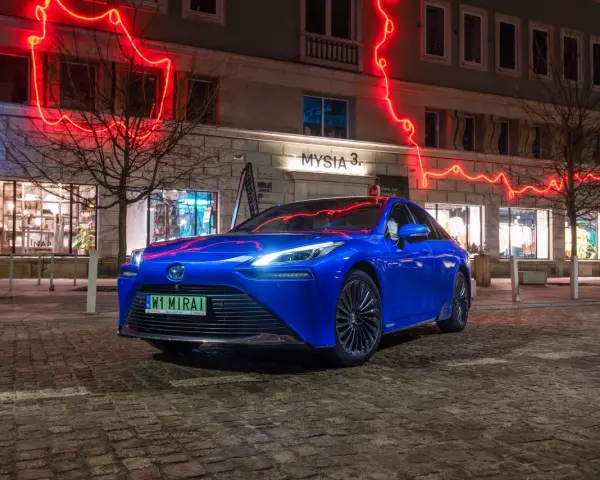 Niebieska Toyota Mirai na nocnej ulicy z neonowym oświetleniem.