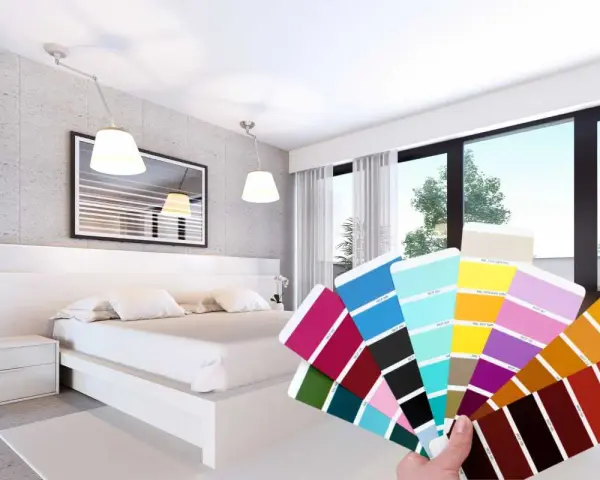 Una mano tiene un campionario di colori davanti a una moderna camera da letto bicolore, con pareti grigie e bianche e un letto bianco.