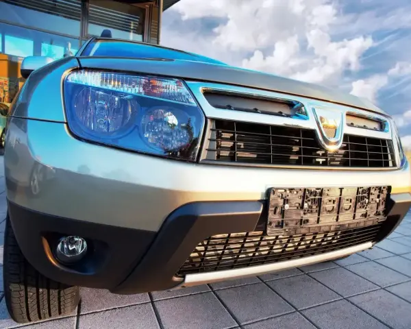 Złoty Dacia Duster 1.6 benzyna z chromowanym grillem i niebieskimi reflektorami, gotowy na przygodę pod błękitnym niebem.