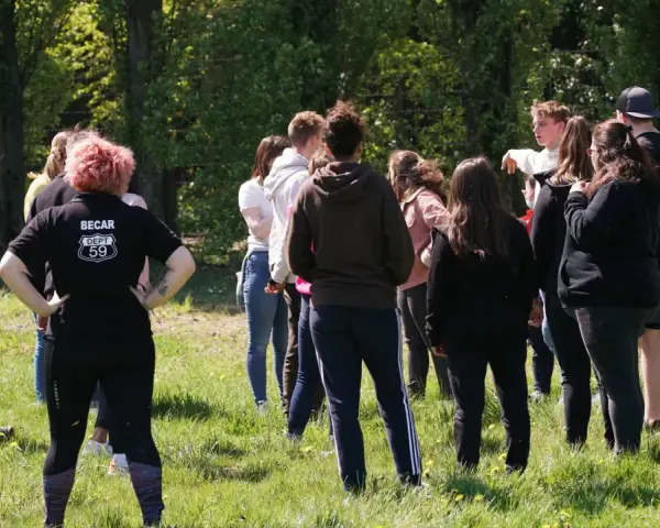 Groupe de jeunes adultes debout dans un champ verdoyant, certains se regardent.