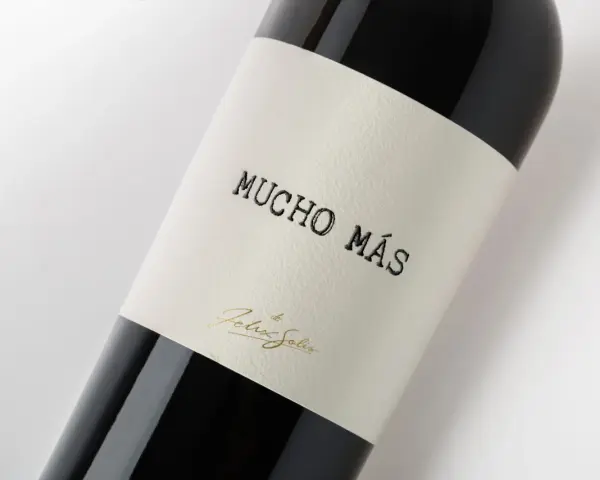 Ciemna butelka wina Mucho Mas, z etykietą z napisem "Mucho Más" i złotym podpisem "Felix Solis".