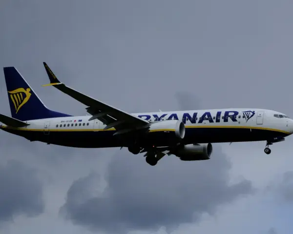 Samolot Ryanair z logo na ogonie leci na tle pochmurnego nieba. Może to być symbol zmiany nazwiska, gdy pasażerowie zmieniają swoje dane przed podróżą.