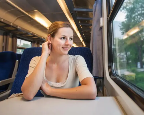 Uśmiechnięta kobieta siedzi w pociągu i patrzy przez okno na krajobraz.