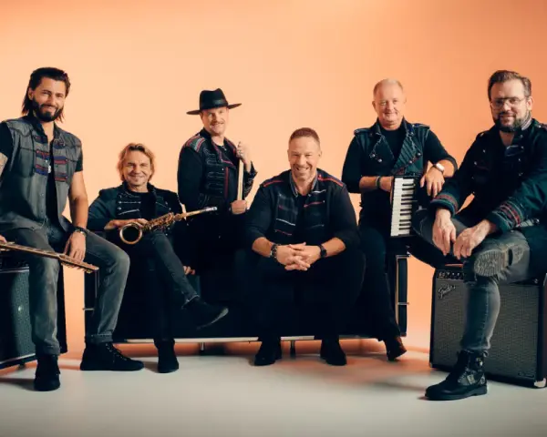 Sechs Männer einer Band posieren vor orangefarbenem Hintergrund, einige sitzen, einer steht.
