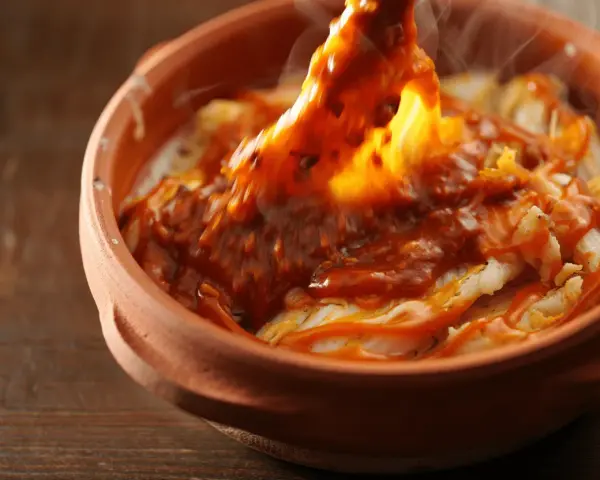 Cocochas de bacalao cubiertas con una salsa roja y burbujeante en una cazuela de barro.