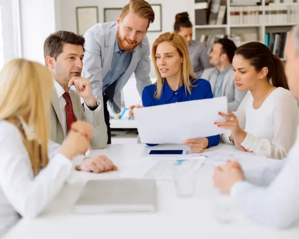 A diverse group of professionals discusses documents, possibly during board of directors recruitment or a strategic meeting.