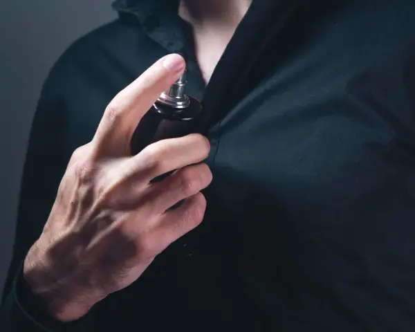 Mann sprüht sich Parfum auf die Brust.