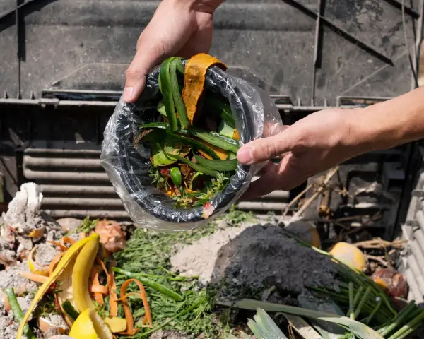 Ręce wsypują do kompostownika resztki roślinne, tworząc cenny nawóz organiczny z odpadów roślinnych.