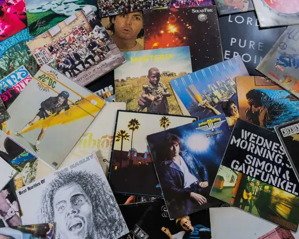 Eine bunte Sammlung von Schallplatten zeigt, welche Musikarten es gibt: Rock von AC/DC, Pop von Genesis, Folk von Simon & Garfunkel und Reggae von Bob Marley.