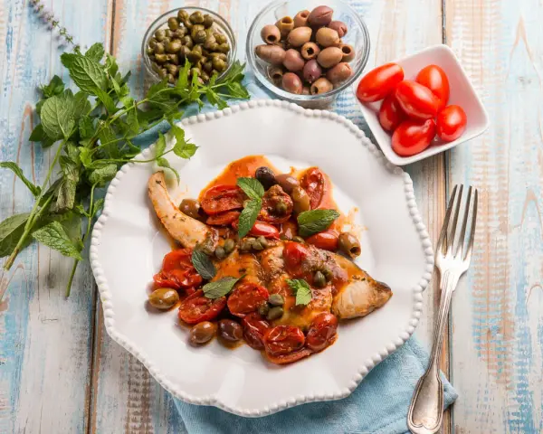 Un saporito pesce spada alla siciliana, condito con pomodorini, olive e capperi, guarnito con menta fresca.