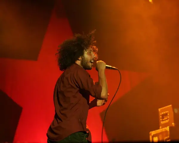 Zac Zack de la Rocha śpiewa z pasją na koncercie Rage Against the Machine. Czerwona gwiazda w tle podkreśla energię występu.