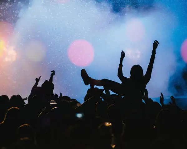 Tłum na jednym z największych festiwali muzycznych na świecie. Kobieta na rękach, ręce w górze, światła sceny.