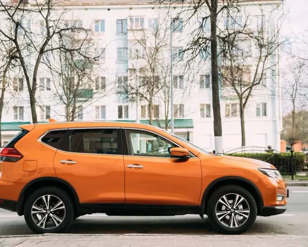 Pomarańczowy SUV do 50 tys. zaparkowany na tle białego budynku i drzew.