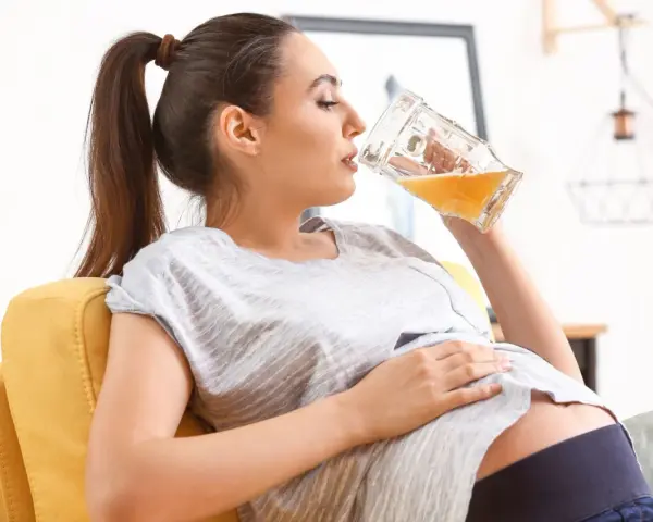 Kobieta w ciąży relaksuje się na kanapie, pijąc piwo bezalkoholowe.