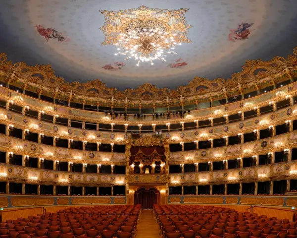 Interno sfarzoso del teatro La Fenice a Venezia, con palchi dorati, affreschi sul soffitto e un lampadario scintillante.