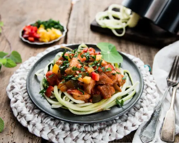 Spaghetti z cukinii z kurczakiem i warzywami w sosie na talerzu.