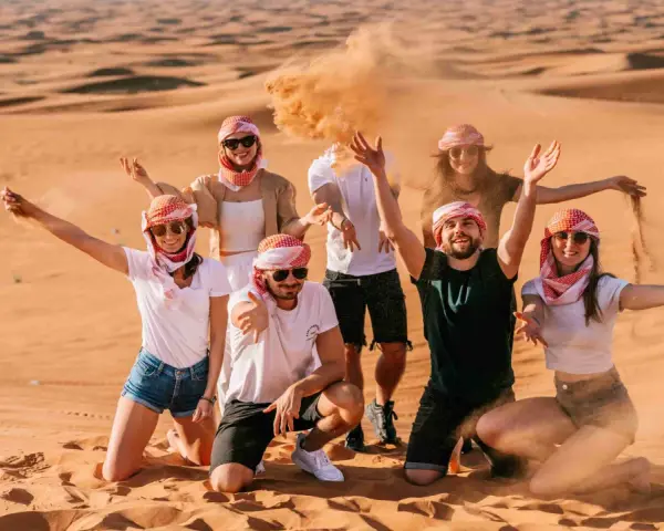 Grupa przyjaciół w tradycyjnych arabskich chustach bawi się piaskiem na pustyni. Wspaniałe wspomnienia z Dubaju w styczniu.