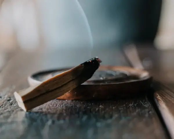 Un palo santo humeante sobre un plato de madera, parte de un ritual de limpieza.