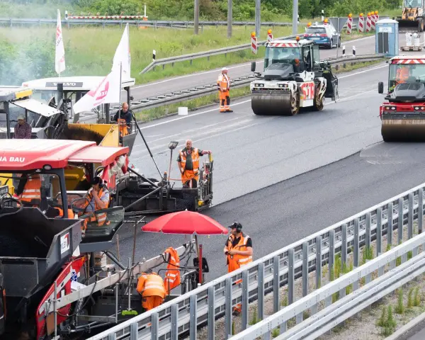 Arbeiter legen auf der ADAC A2 mit Maschinen und Walzen neuen Asphalt.