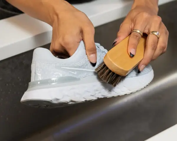 Mani che puliscono una scarpa da ginnastica bianca con una spazzola, mostrando come lavare le tn bianche per farle tornare come nuove.