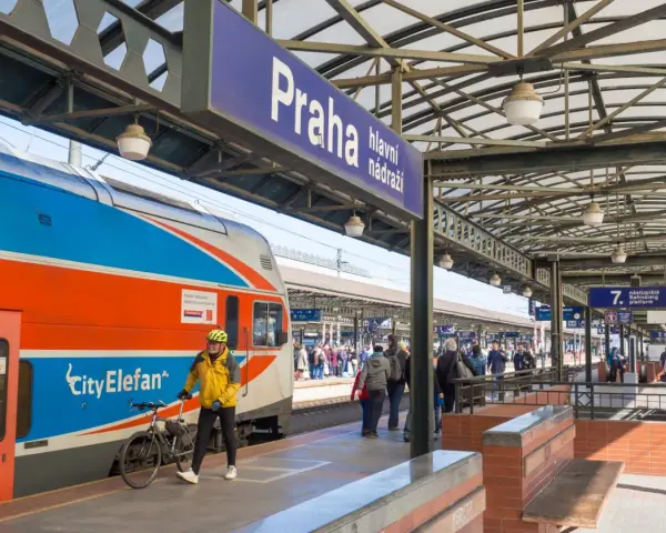 Pociąg z Gdańska do Pragi na dworcu głównym. Mężczyzna w żółtej kurtce z rowerem czeka na peronie.