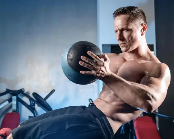Un homme transpire en faisant un exercice oblique avec un ballon de médecine dans une salle de sport.