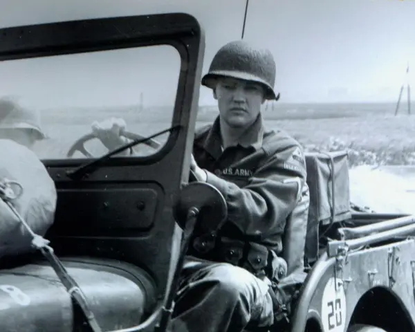 Elvis Presley in seiner US Army Uniform, sitzt am Steuer eines Jeeps.