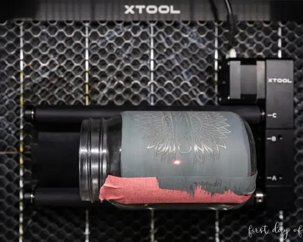 Laser engraving a jar with tempera paint. The laser is creating a sunflower design on the painted glass.
