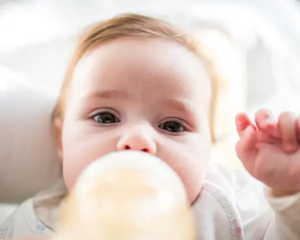 Urocze niemowlę pije mleko z butelki. Ważne, by mleko miało odpowiednie ile stopni mleko dla niemowlaka, by było bezpieczne i smaczne.