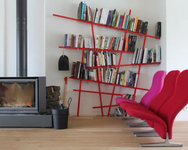 Camino acceso, attrezzi da camino, e moderne piccole librerie rosse piene di libri, con sedie colorate.