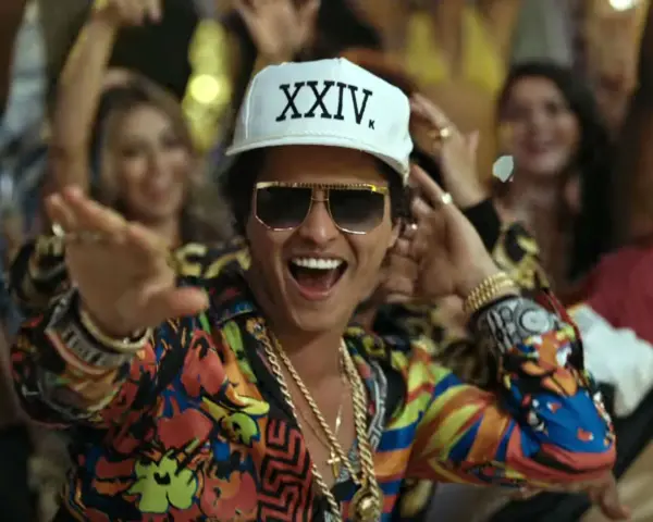 Bruno Mars w Polsce! Wesoły artysta w kolorowej koszuli i czapce z napisem "XXIV K" tańczy wśród rozbawionych ludzi.