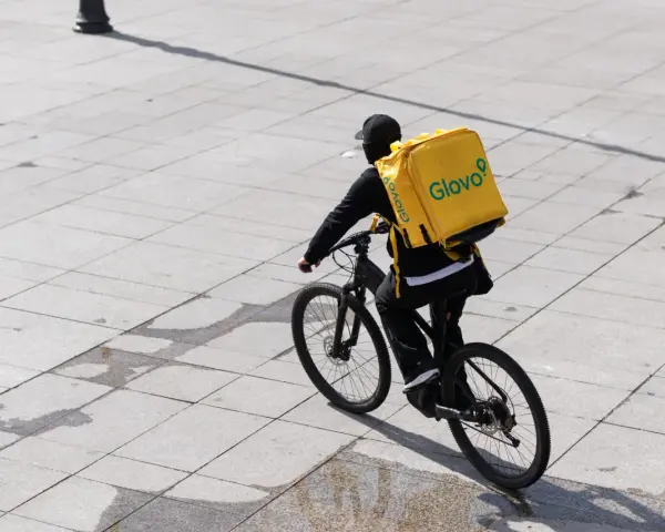 Kurier Glovo na rowerze z charakterystyczną żółtą torbą. Praca w dostawie to jego codzienne wyzwanie.