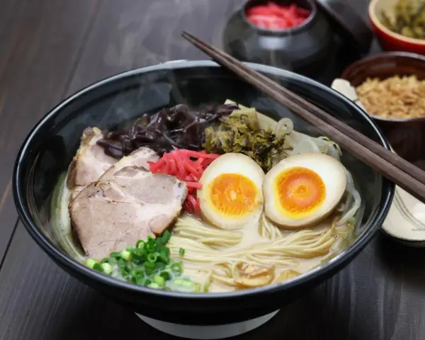 Pyszny ramen co to? Aromatyczny bulion, makaron, plastry wieprzowiny, jajko na pół, szczypiorek i marynowane dodatki.