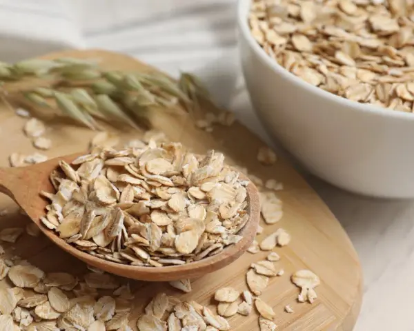 Płatki owsiane na drewnianej łyżce i w misce. Czy płatki owsiane mają gluten? Czysty owies jest bezglutenowy, ale warto sprawdzić etykietę.