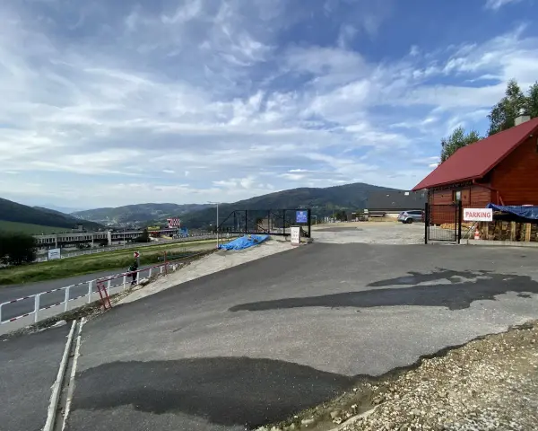 Widok na parking przy górze Żar. W oddali widać zabudowania i góry.