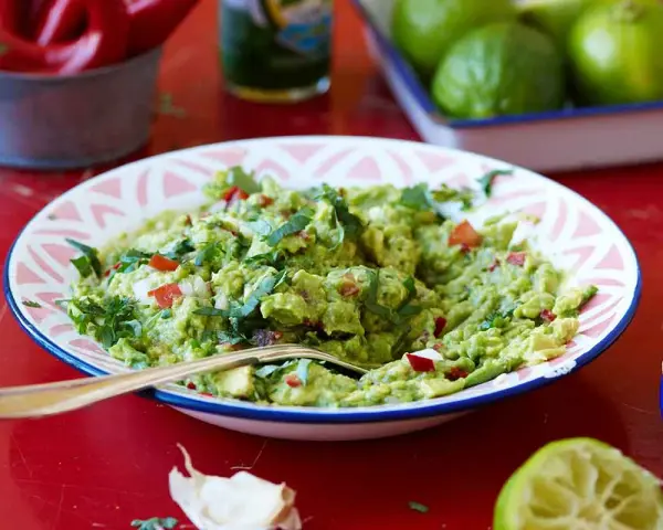 En skål med krämig guacamole, perfekt för ditt nästa guacamole recept. Serveras med tortillabröd, lime och chili.