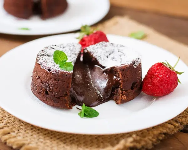 Pyszny fondant czekoladowy z płynnym środkiem, przypominający małe soufflé czekoladowe, podany z truskawkami i miętą.