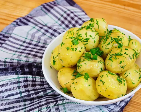 Młode ziemniaki w misce, posypane koperkiem i szczypiorkiem. Idealne na lato, a ile gotować młode ziemniaki? Krótko!