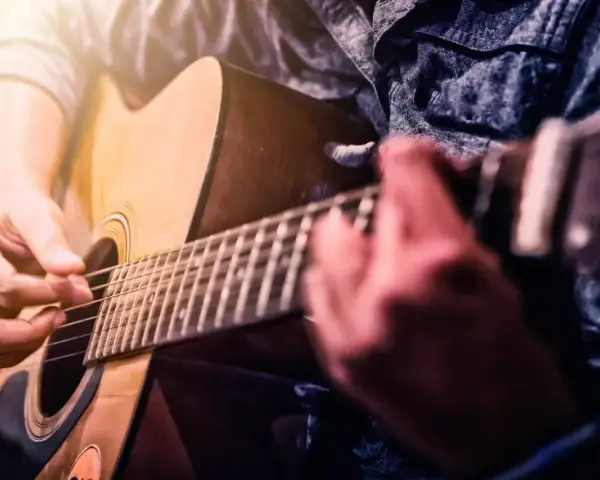 Ręce grające na gitarze akustycznej. Idealne dla tych, którzy zaczynają swoją przygodę z nauką gry na gitarze dla początkujących.