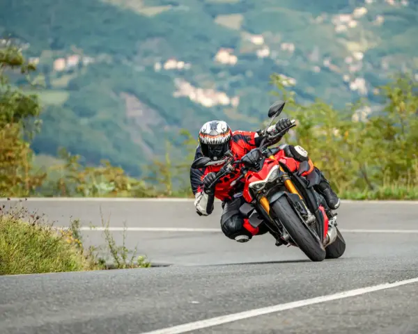 Un motociclista esperto piega in una curva stretta, con il ginocchio quasi a terra, affrontando un passo in montagna.