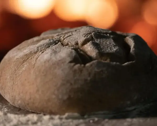 Ein Laib Brot liegt auf einer bemehlten Holzschaufel, bereit für den Ofen. So gelingt energiesparend Brot backen.