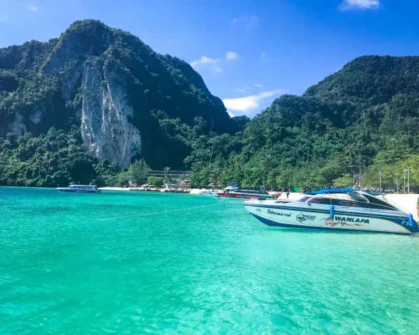 Turkusowa woda i łodzie motorowe przy plaży w Maya Bay. W tle zielone, skaliste góry.