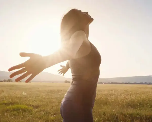 Frau mit ausgebreiteten Armen im Sonnenlicht, ein Symbol für das Heilen von Hypochondrie und das Finden von innerem Frieden.