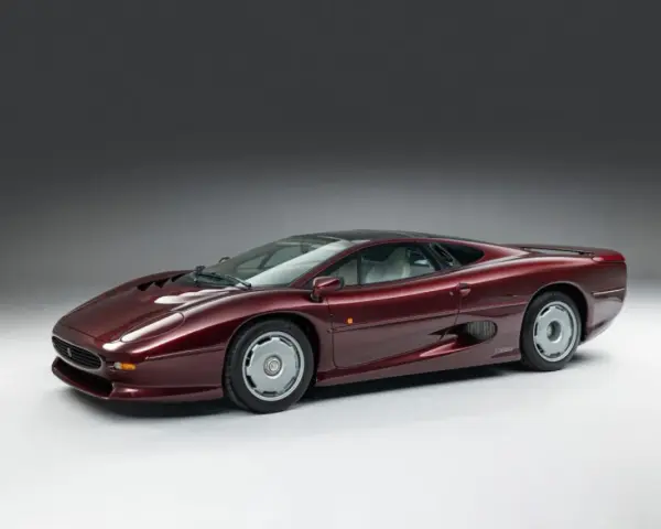 Bordowy Jaguar XJ220, ikona motoryzacji lat 90., prezentuje swoje aerodynamiczne linie na tle szarego tła.